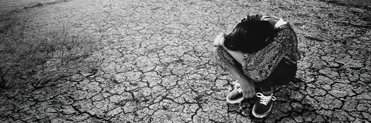 A woman sitting on broken ground, representing the weight and fragmentation of living with depression